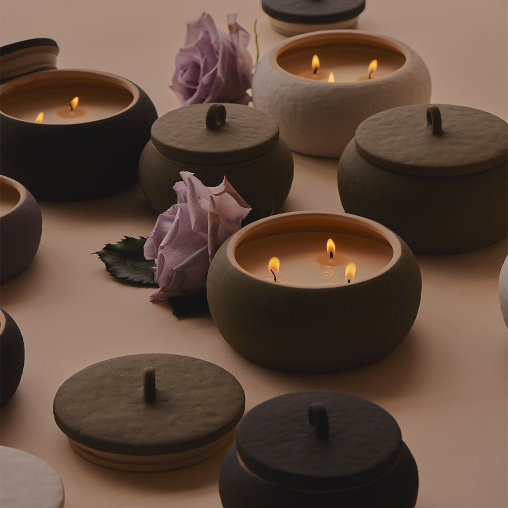 A photo of three lit candles from the Cali collection on a beige background among flowers.