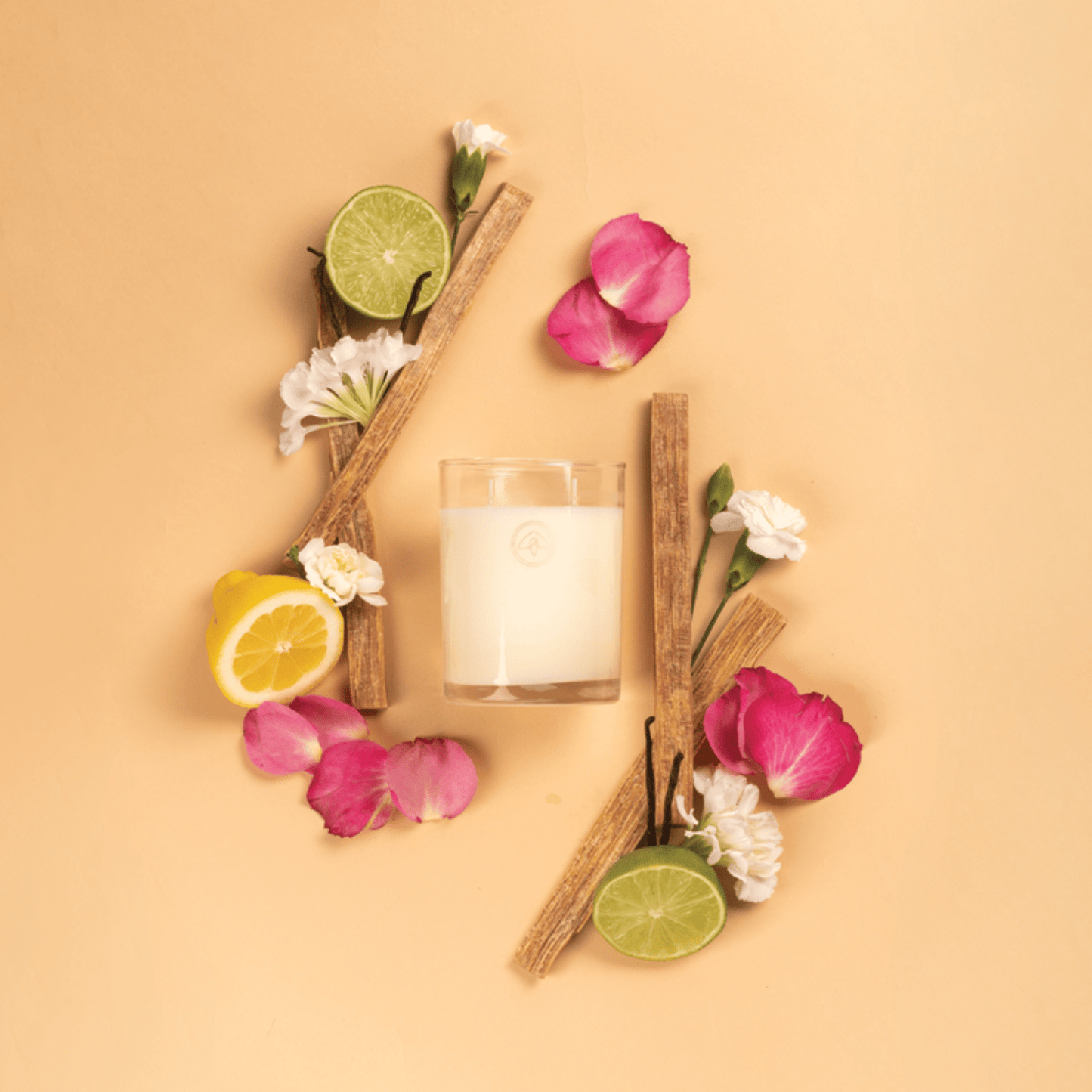 Clarity Enchanted Rose candle on a peach background surrounded by rose petals, sandalwood, lime and lemon