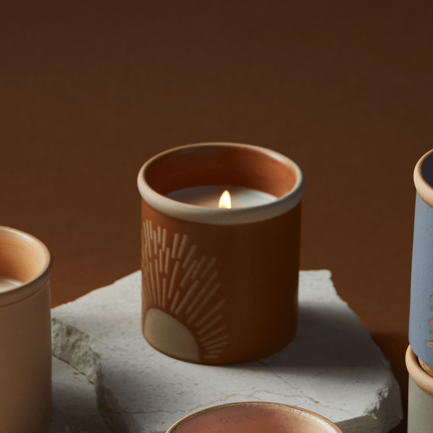 8 oz orange ceramic vessel with sun design and cork lid (also containing sun design); lid off, lit