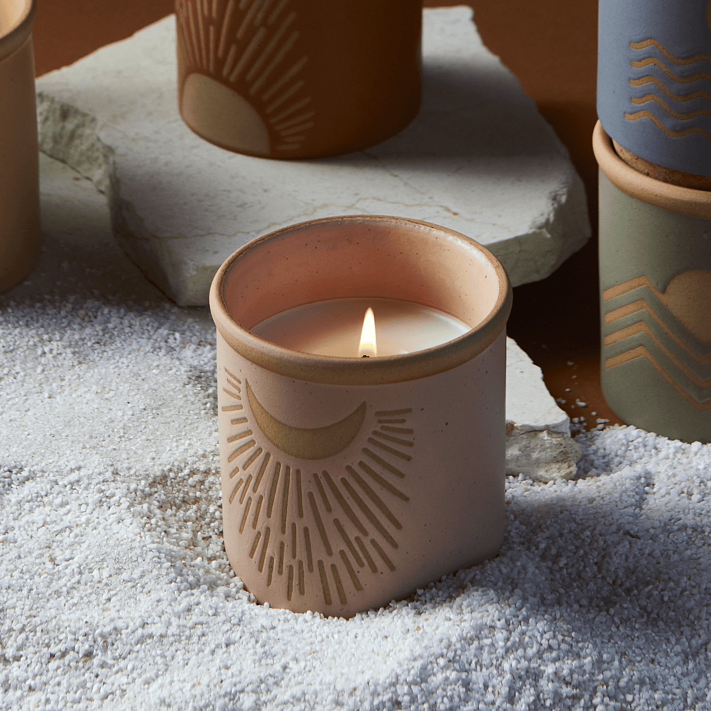 8 oz pink ceramic vessel with moon design and a cork lid (also containing the same design); pictured lit with other candles