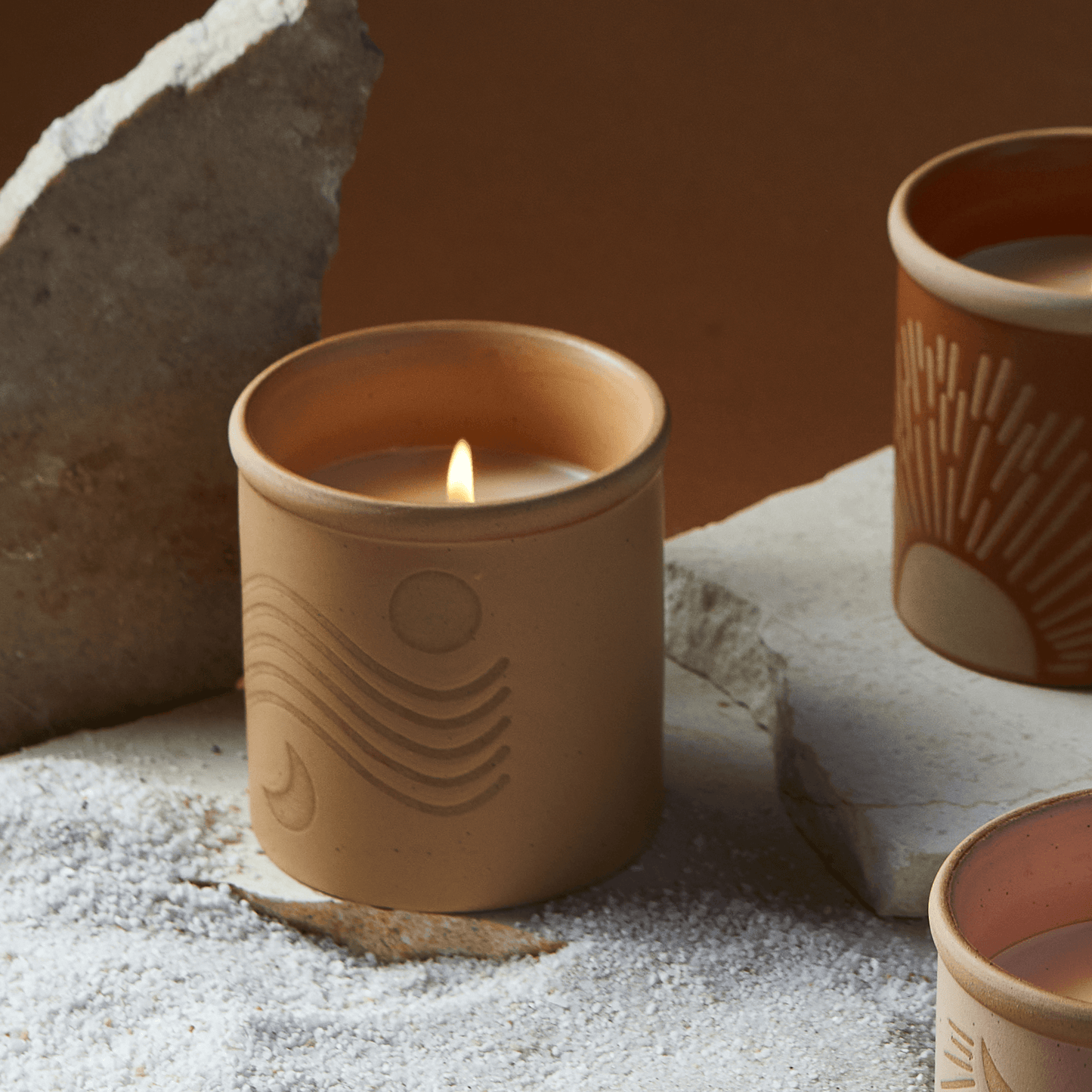 8 oz yellow ceramic vessel with sun/moon design and a cork lid (also containing the same design); pictured lit with other candles