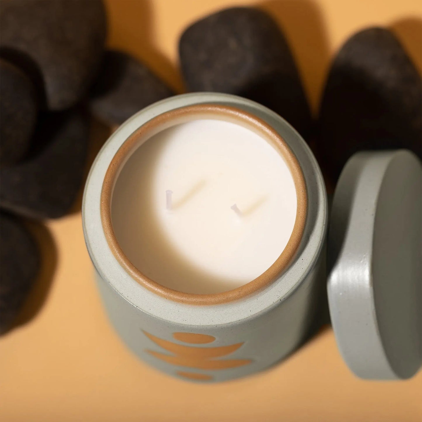 12 oz blue cylindrical ceramic vessel with ceramic lid; white wax and two cotton wicks; reflected beige design on the side; pictured with lid off