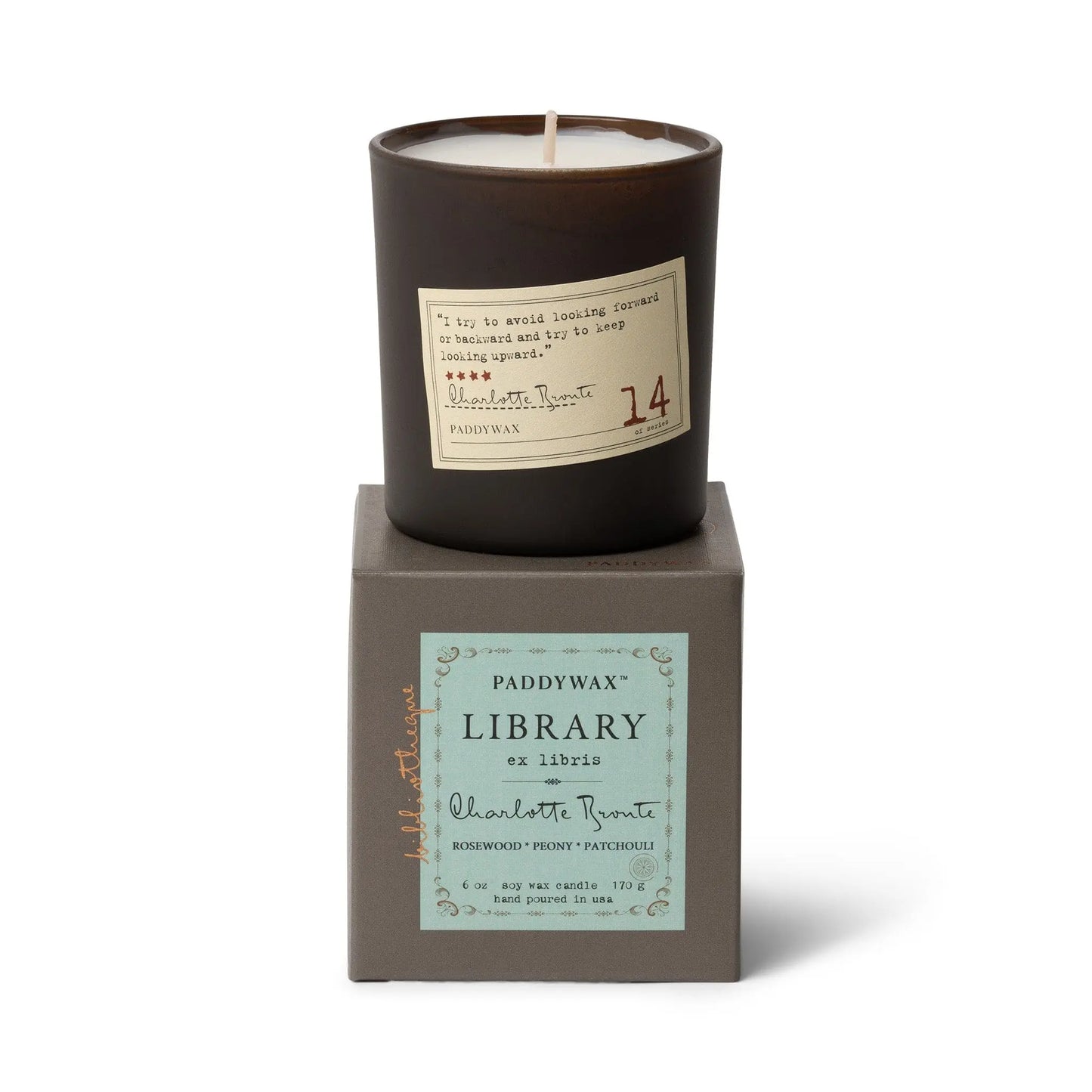 A black candle in a brown glass holder rests on a gray box labeled “Library 6 oz Candle - Charlotte Bronte,” featuring Rosewood, Plum, and Patchouli scents inspired by literary classics.