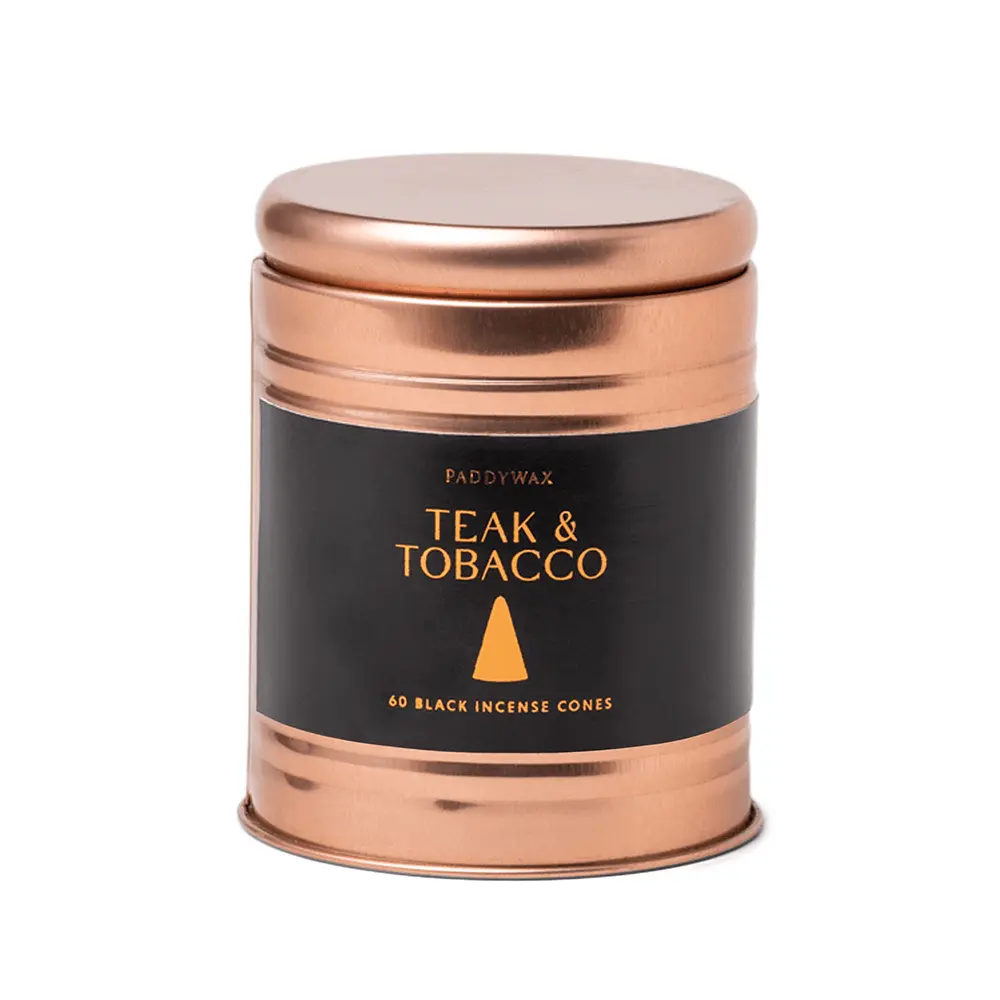 A copper-colored tin labeled Incense Cone - Teak & Tobacco holds 60 black cones by Paddywax, ideal for enjoying flameless fragrance in your space.