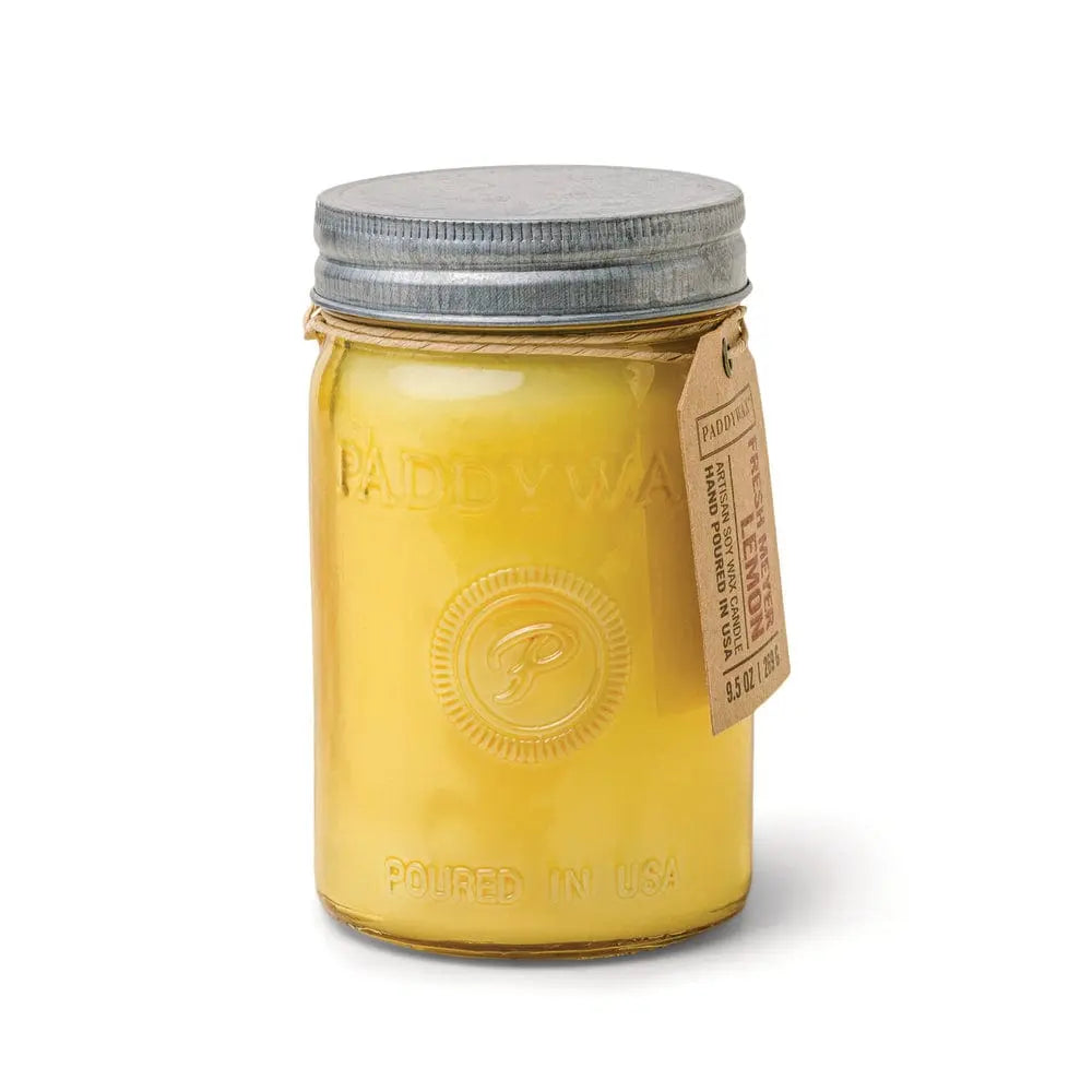 The Relish 9.5 oz. Candle - Fresh Meyer Lemon comes in a yellow glass mason jar with a metal lid and brown tag, embossed with Paddywax and Poured in USA, adding charm and fresh fragrance to your space.