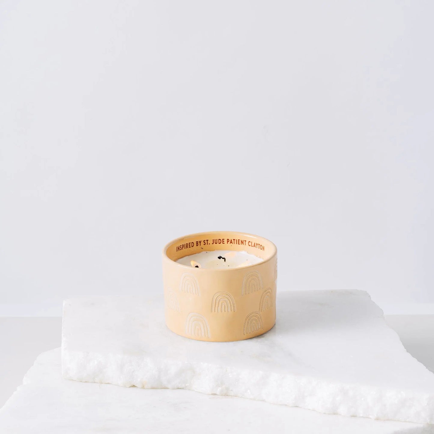 Yellow ceramic candle with rainbows and white soy wax center with three wicks burning