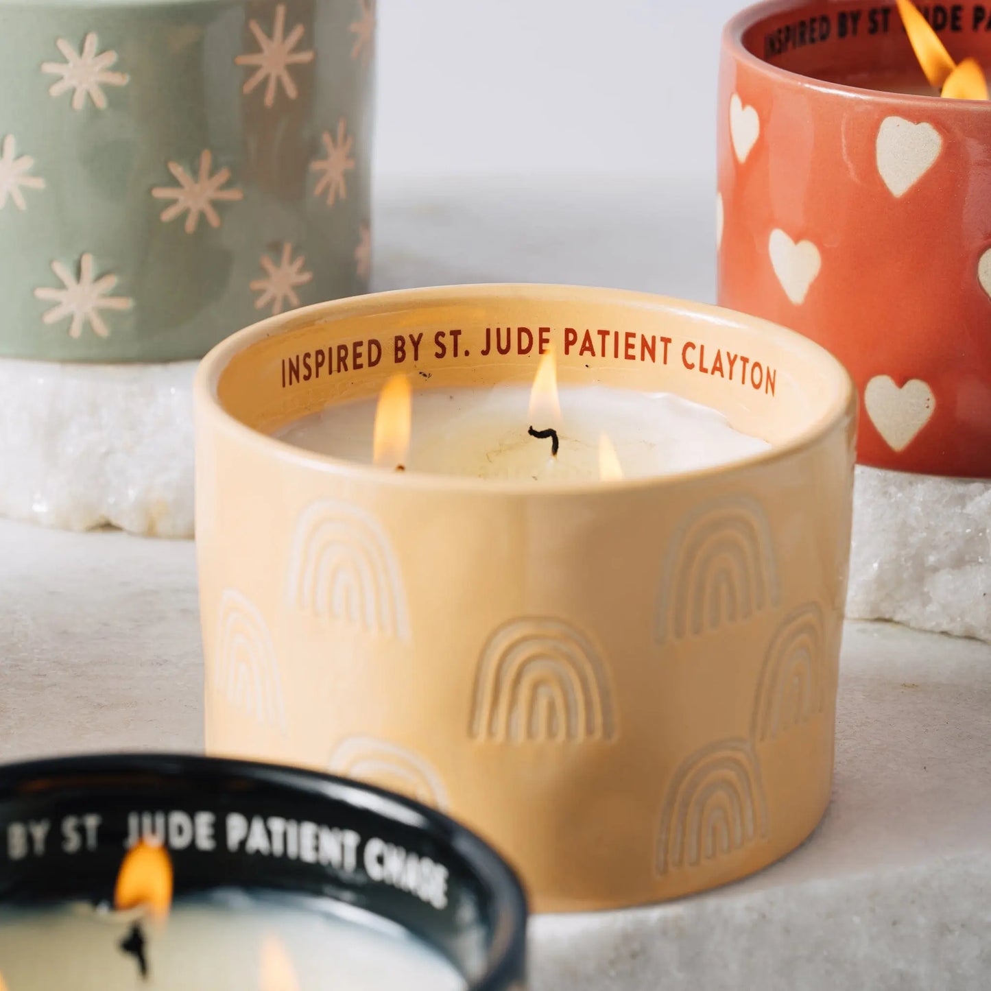Group shot of St. Jude candle collection with yellow ceramic candle burning in main focus.