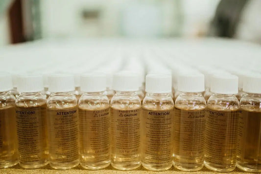 A row of clear plastic bottles filled with liquid, each labeled with cautionary text in both English and French.