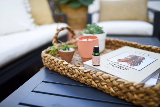 A cozy outdoor setting with a woven tray, potted plants, a candle, a bottle of bug repellent, and a book titled CITY SURF.