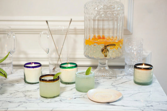 A marble countertop with colorful candles, a water dispenser with citrus slices, and a small plate on the side.