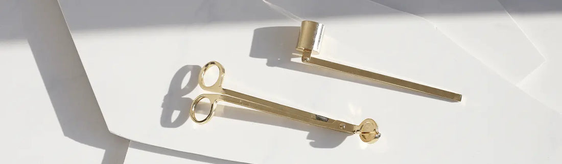 Two gold-colored tools on a white surface, with one resembling a pair of tongs and the other a straight bar tool, casting shadows