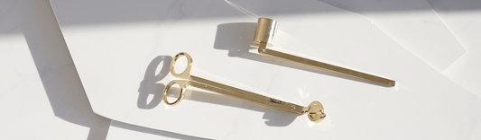 Two gold-colored tools on a white surface, with one resembling a pair of tongs and the other a straight bar tool, casting shadows