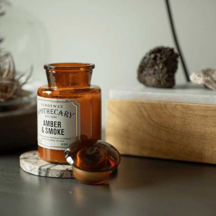 Apothecary Amber Smoke candle on a side table amongst knick knacks