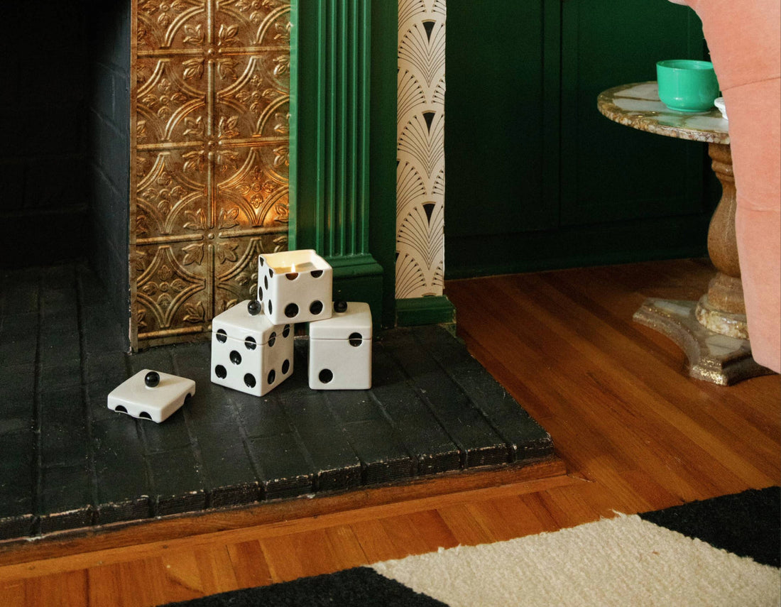 Three dice-shaped ceramic containers stacked on a black fireplace hearth, with one lid set aside.