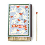 A Dopo Flower - 75ct Boxed Matches feature white doves and red flowers on the lid, ideal for lighting your A Dopo candle or recalling Mediterranean travels. Shown with a single red-tipped matchstick.