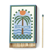 A Dopo Palm Tree - 75ct Boxed Matches features a Mediterranean-inspired palm tree and sun design; the partially open box reveals wooden safety matches, with one match placed beside it.