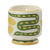 The Wild Lemongrass - A Dopo 8 oz Candle is a lit ceramic candle in a holder with green snake and yellow designs on white, blending artistic charm and Mediterranean fragrance.