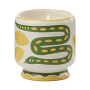 The Wild Lemongrass - A Dopo 8 oz Candle is a lit ceramic candle in a holder with green snake and yellow designs on white, blending artistic charm and Mediterranean fragrance.