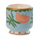 The A Dopo Flower Candle - Cactus Flower features a lit ceramic candle in a blue holder, hand-painted with orange flowers and green leaves.