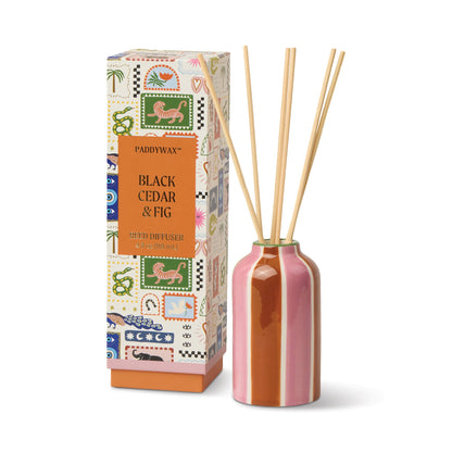 The Black Cedar & Fig - A Dopo 4 oz Diffuser features a pink and brown striped ceramic bottle with four wooden reeds, beside a vibrant box adorned with animal illustrations.