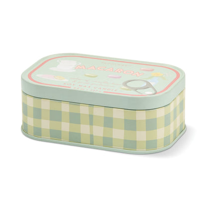The Macaron - Bistro 4.5 oz Tin Candle comes in a rectangular tin adorned with a green and cream plaid pattern and is labeled “Macaron” on the lid. The soy wax candle is infused with a delightful macaron fragrance, capturing the essence of a Parisian café. Decorative teacup, plate, and floral illustrations on the lid add an elegant touch, making this French-inspired candle both stylish and inviting.