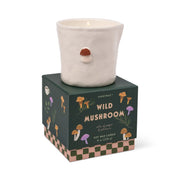 The Wild Mushroom - Bistro 8 oz Candle comes in a white ceramic holder with a small mushroom detail, atop a dark green box adorned with mushroom art and a pink checkerboard border—perfect for displaying or enjoying bistro candles.