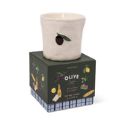 The Fig & Olive - Bistro Candle 8 oz, a white ceramic candle holder with an olive design, rests on its box decorated with olives, olive oil, bread, and lemons—perfect for bistro or hand-painted ceramic candles.