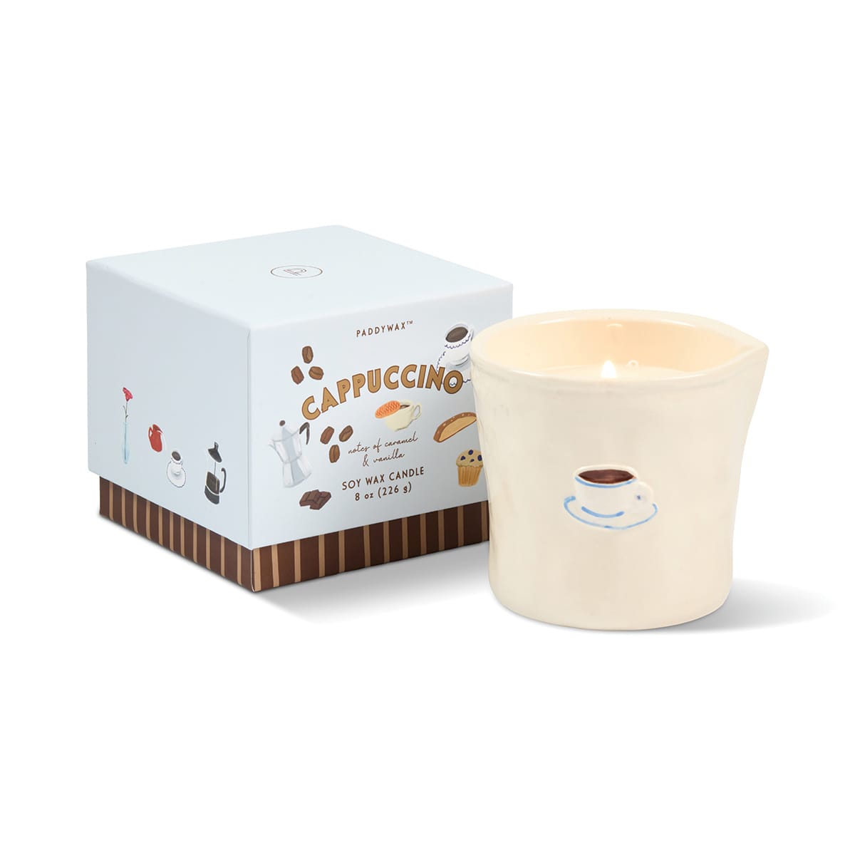 A lit Cappuccino - Bistro 8 oz Candle, housed in a cream-colored reusable ceramic vessel featuring a coffee cup illustration, sits beside a box labeled “Cappuccino” adorned with coffee-themed graphics. This bistro ceramic candle infuses any space with cozy café vibes.