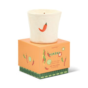A white ceramic candle holder featuring a red chili pepper motif rests atop an orange box adorned with illustrations of peppers and limes. The bistro-inspired design adds a delightful touch, while the packaging reads “Piment - Bistro 8 oz Candle, soy wax (226 g),” hinting at the distinctive Piment fragrance inside.