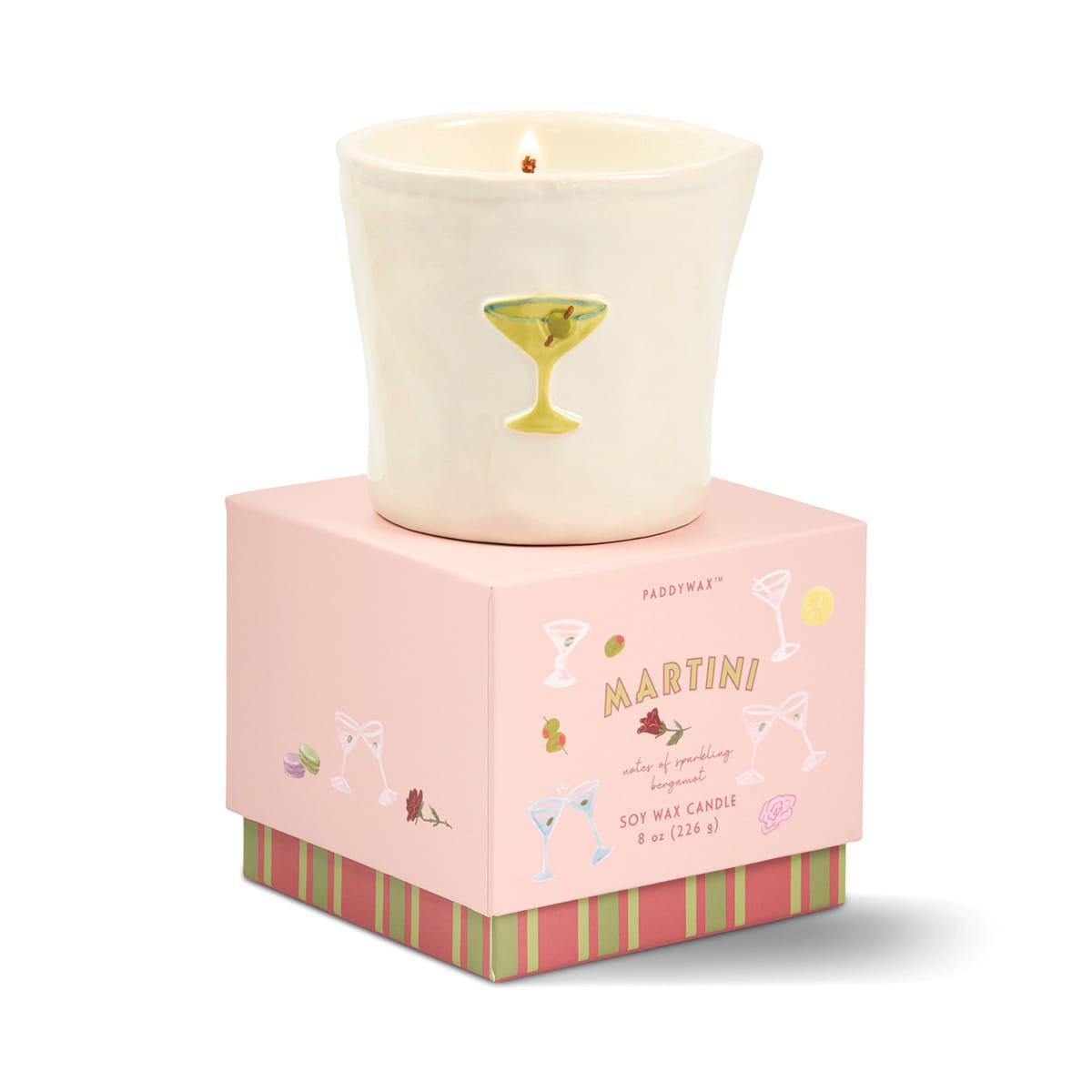 A lit white candle in a ceramic cup featuring a martini glass design rests on top of a pink box labeled “Martini - Bistro 8 oz Candle.” The packaging is adorned with cocktail glass illustrations and decorative stripes.
