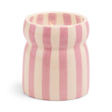 The Grecian Sand - Cabana 6.5 oz Candle features a ceramic vessel with vertical pink and white stripes, holding a lit candle that's ideal for displaying hand painted candles or adding refreshing coastal scents to your space.