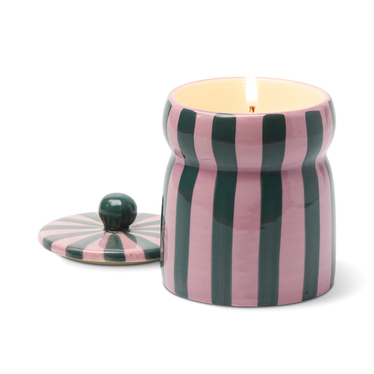 The Cinnamon & Clove - Cabana 6.5 oz Candle is lit, displayed in a pink and green vertically striped ceramic jar, with the matching lid set beside it on a white background.