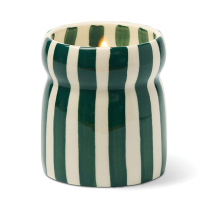 The Isla Fresca - Cabana 6.5 oz Candle is a ceramic candle holder with vertical green and white stripes, holding a lit candle.