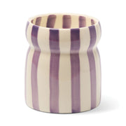 A 6.5 oz Waikiki Waters - Cabana candle, housed in an elegant ceramic vessel with a rounded rim and a smooth, glossy finish, featuring vertical purple and white stripes—evoking the refreshing ambiance of Waikiki Waters.