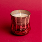Elevated view of a lit Cypress & Fir - 9oz Frosted & Shiny Copper Metallic Glass candle on a red background.