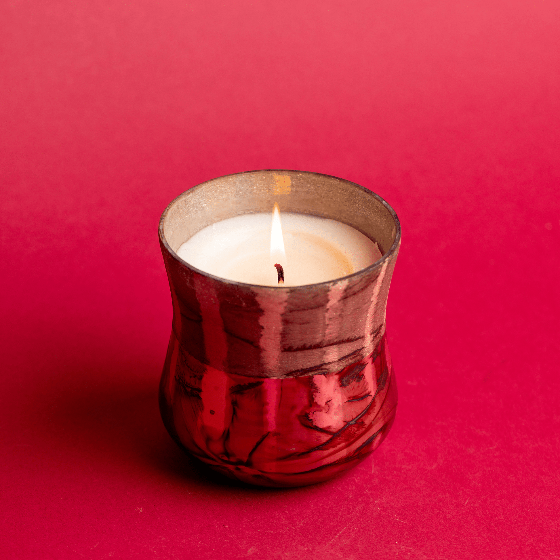 Top view of a lit Cypress & Fir - 9oz Frosted & Shiny Copper Metallic Glass candle on a red background.
