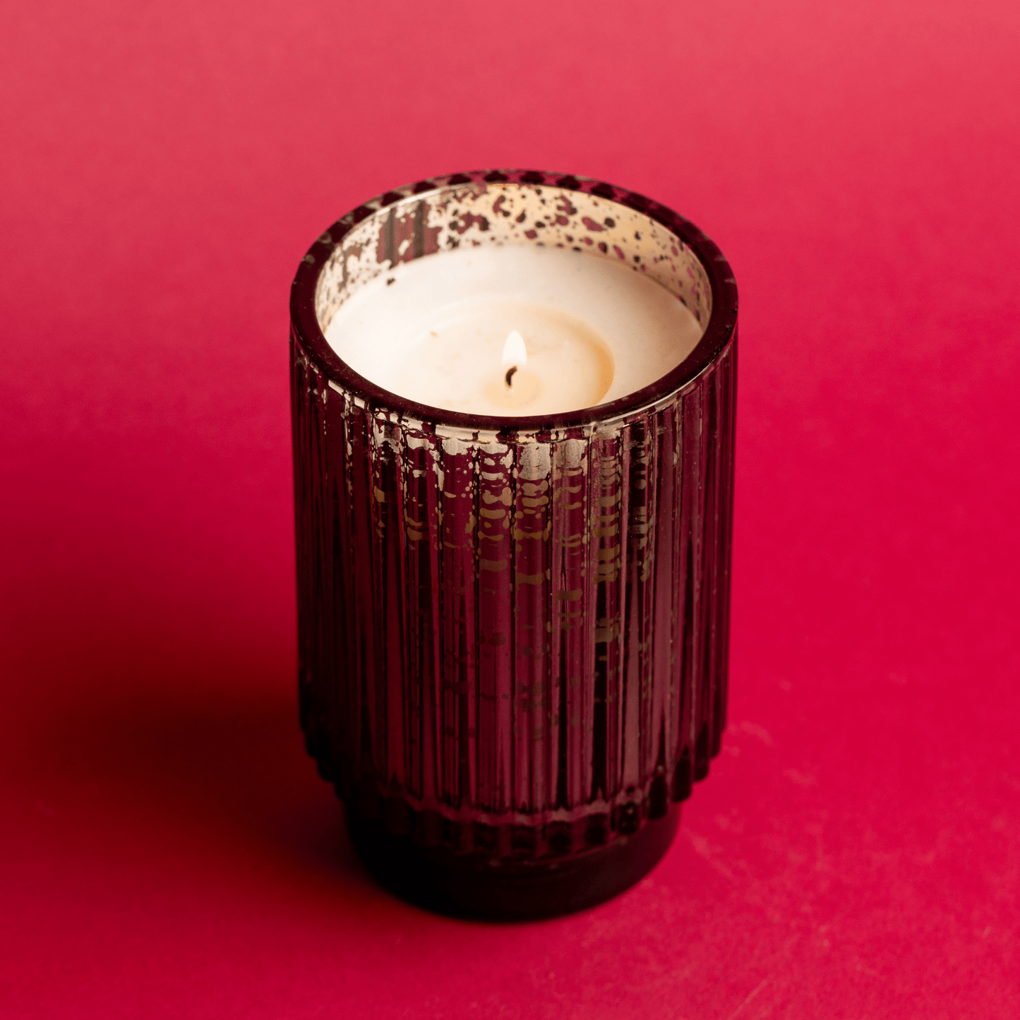 A lit 12 oz. tall mercury glass vessel on red background
