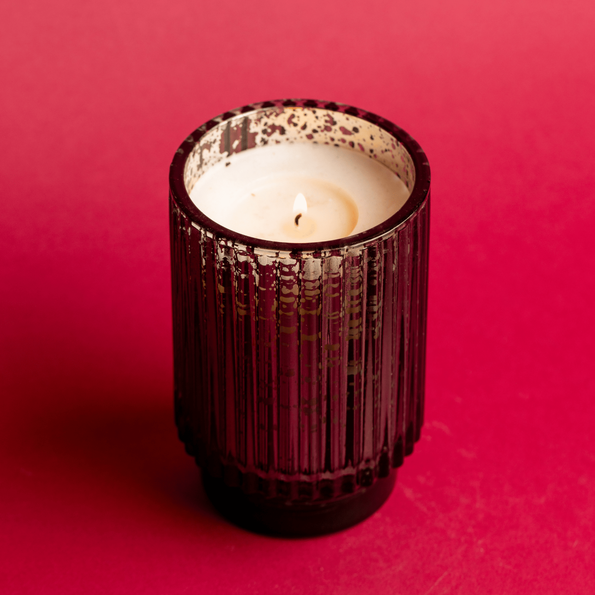 A lit 12 oz. tall mercury glass vessel on red background