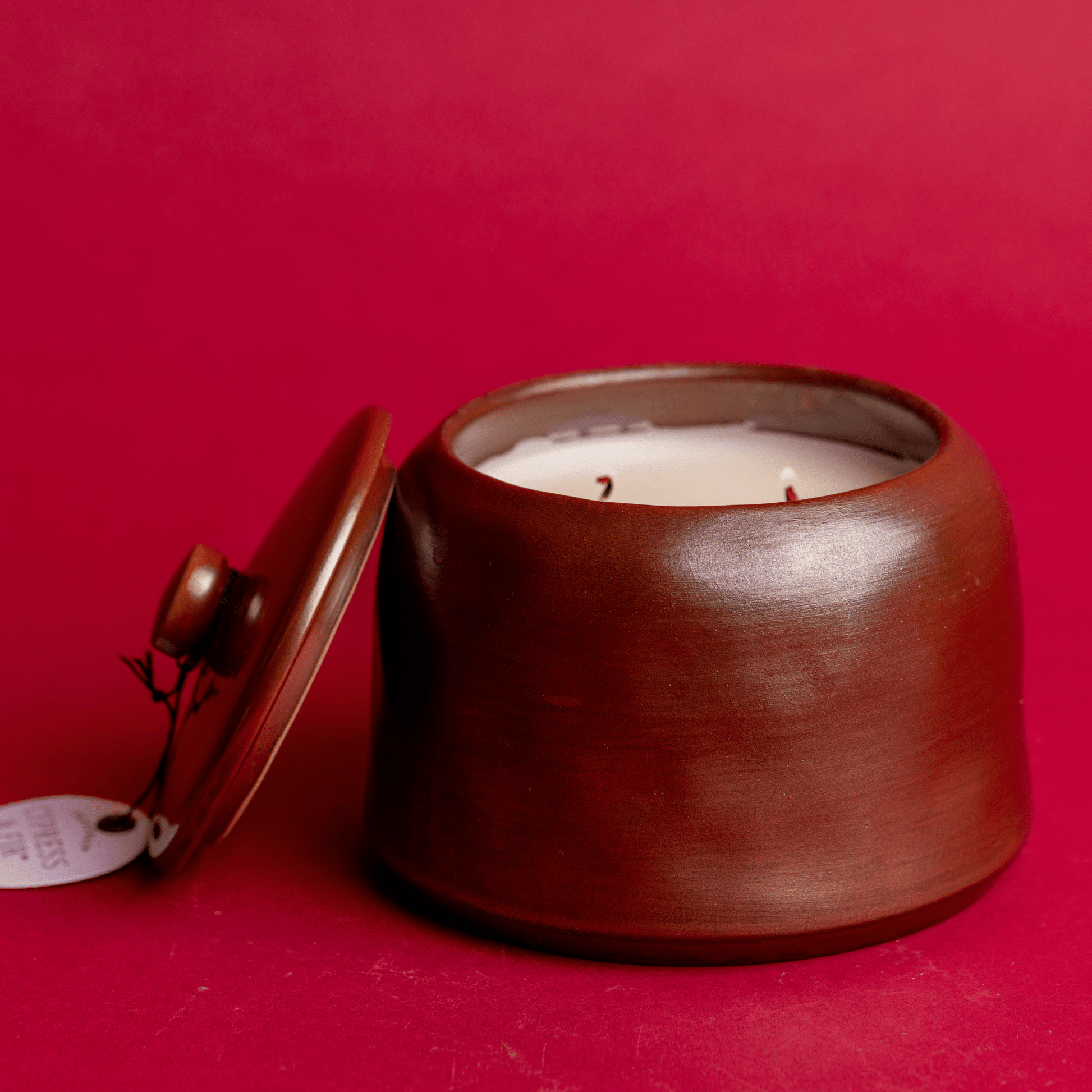 Front view of a lit, two wick Cypress & Fir - 11oz Bronzed Glazed Ceramic Jar candle on a red background
