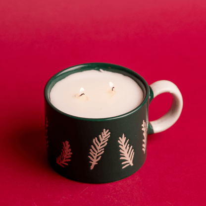 Top angle of lit Cypress & Fir - 8oz Green Ceramic Mug candle on a red background