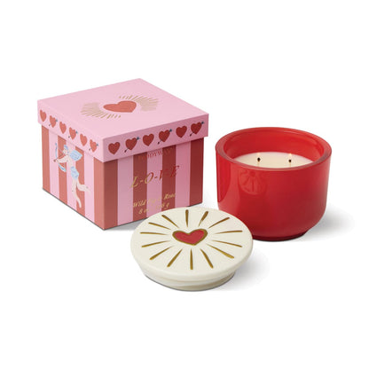 The Wild Fig & Rose - Charmed 8oz Candle, in a ceramic container with a heart-adorned white lid, sits next to a pink and red gift box decorated with hearts and the word LOVE.