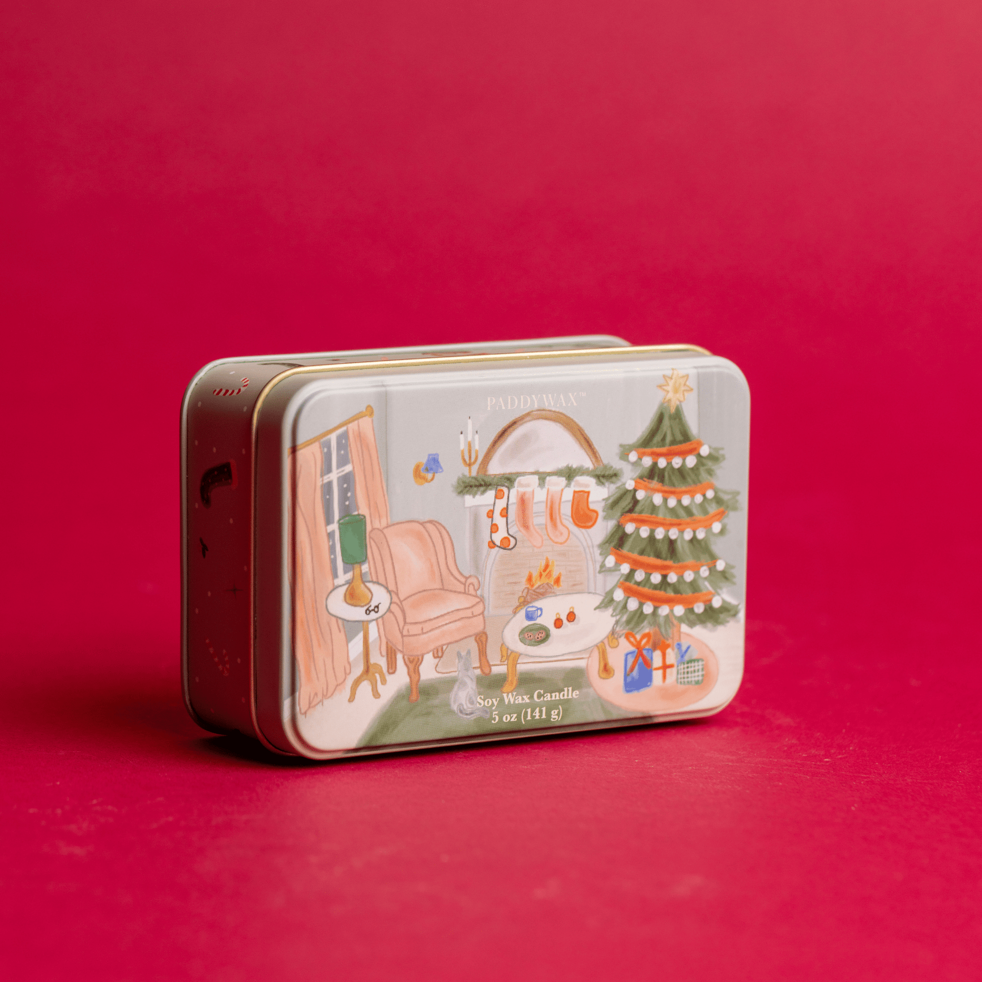 5 oz holiday tin with custom artwork resting on red table and lit