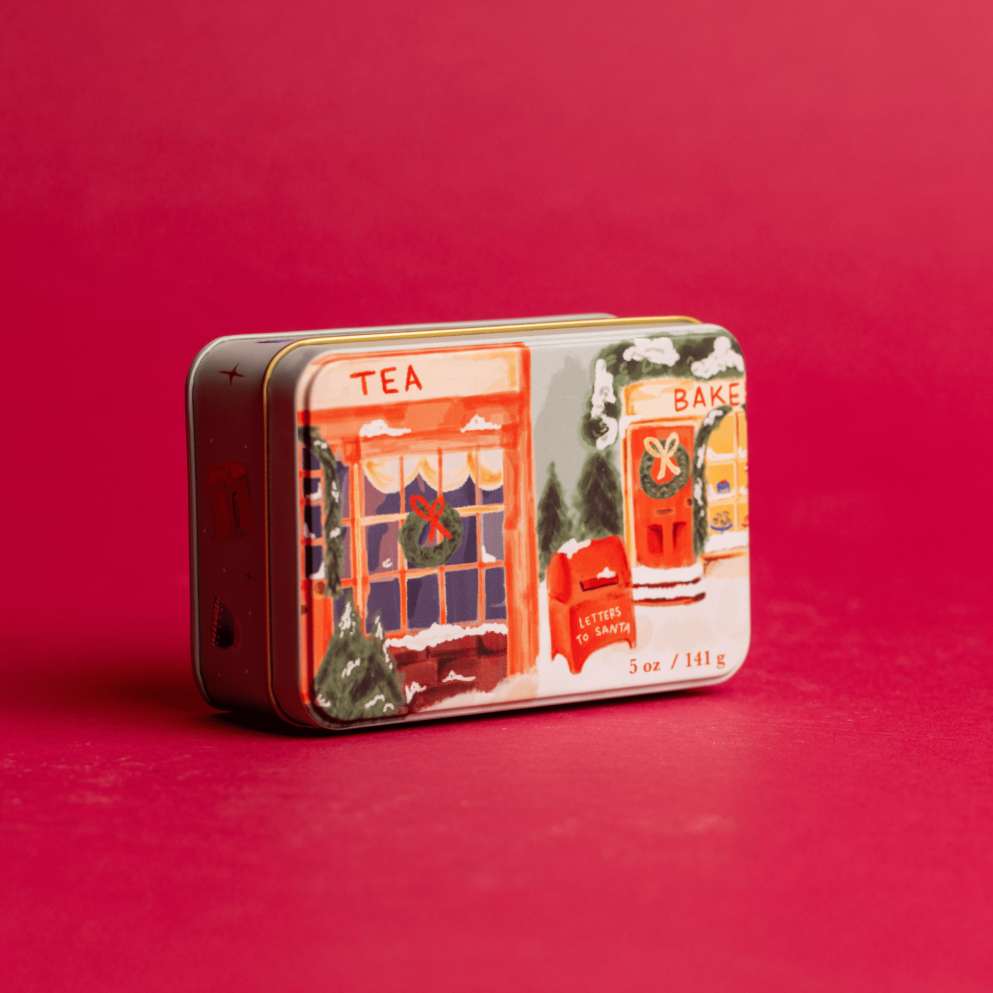 5 oz holiday tin with custom artwork; lid shows snow-covered storefronts on red background