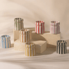 Seven small, striped ceramic vases in various colors are displayed on and around beige rectangular blocks against a neutral background.