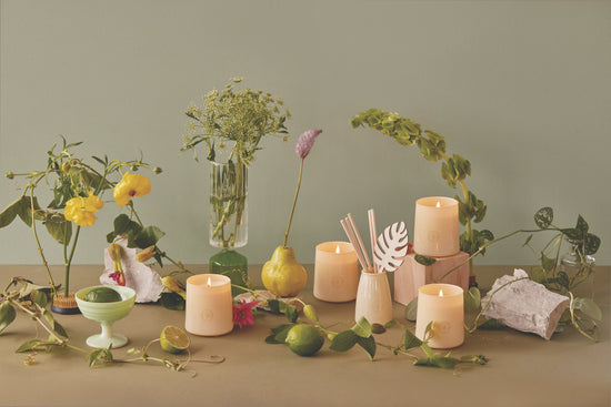 Flourish Candle collection on a table with lots of greenery, flowers, vases, and fruit