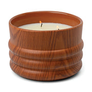 The Redwood & Amber - Grain 12 oz Candle glows with two flickering flames in a round, brown, wood-patterned ceramic container, set against a white background.