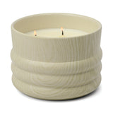 A cream-colored, textured ceramic vessel from the Grain collection holds a 12 oz Hinoki Driftwood candle with two lit wicks.