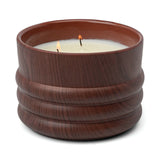 The Bergamot & Mahogany - Grain 12 oz Candle has two wicks and comes in a brown ribbed ceramic jar, part of the Woodgrain Candle Collection. It features notes of bergamot and mahogany.