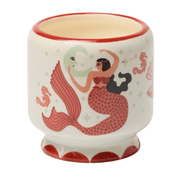 Introducing the Ginger & Teak - A Dopo 8 oz Candle, housed in a white hand-painted ceramic vessel adorned with red trim and an illustration of a mermaid holding a moon mask, surrounded by sea horses and shells. This unique piece is perfect for filling your space with the earthy fragrance of Ginger & Teak.