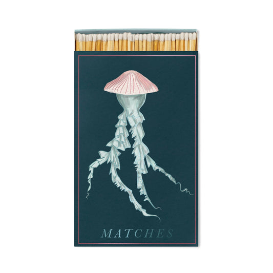 The Jellyfish - Large Rectangle Boxed Matches features a pink and white jellyfish on a dark background—perfect coastal décor or ocean lover gift. MATCHES is in light blue, with matchsticks peeking out at the top.
